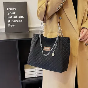 Detail einer großen schwarzen Stepptasche mit silbernen Kettenriemen an einem Model