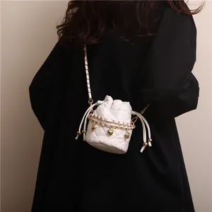 Detailed shot of white quilted bucket bag featuring golden heart pendant and chain strap