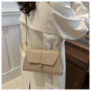Détail d'un sac bandoulière en cuir beige avec boucle ronde en métal doré sur modèle