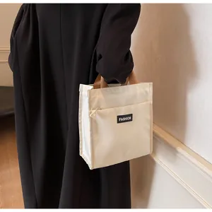 Minimalist beige canvas lunch bag with brown straps and front pocket shown on model