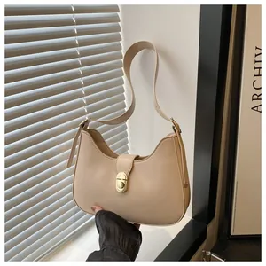 Close-up of beige crescent shoulder bag featuring a golden metallic twist-lock closure