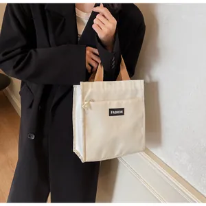 Close-up of a beige nylon lunch bag with brown straps and front pocket shown on a model
