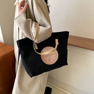 Close-up of a large black canvas tote bag with brown OK YF circular print on model side view