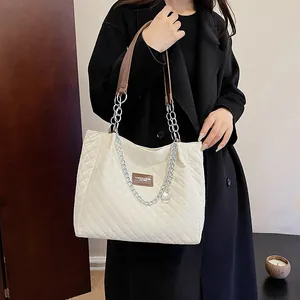 Detailansicht der beigen Stepptasche mit braunem Ledergriff und silberner Metallkette
