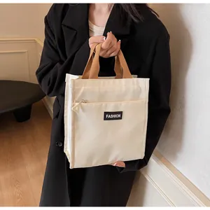 Close-up of cream canvas lunch bag with 'FASHION' patch and brown webbing handle