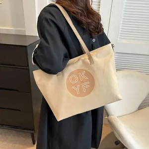 Rear view of a beige canvas tote bag with circular letter print on a female model
