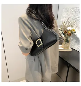 Modella indossa borsa baguette nera con trama screpolata e grande fibbia dorata