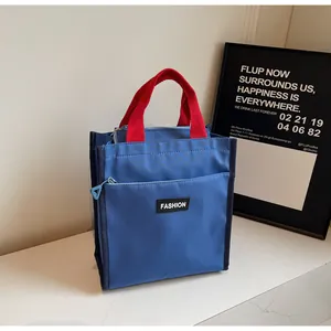 Close-up of blue nylon tote bag with red handles and fashion label detail on front pocket
