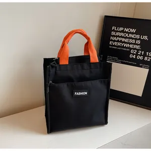Detail of the black canvas tote bag showing the orange handles and fashion label detail