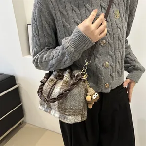 Detail of wool bucket bag with checkered pattern, woven handle and plush charm on model