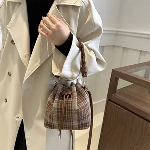 Detail of tweed bucket bag featuring brown braided handle and leather drawstring closure