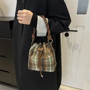 Detailed view of bucket bag featuring plaid wool fabric and woven leather handle