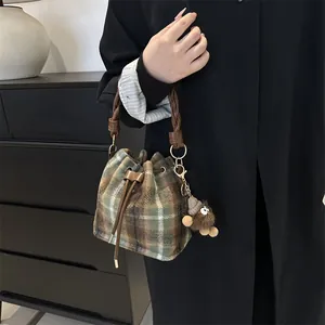 Detail of plaid bucket bag with forest green pattern, plush charm and braided handle