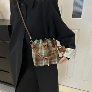 Detail of plaid bucket bag with drawstring closure and plush pendant on model