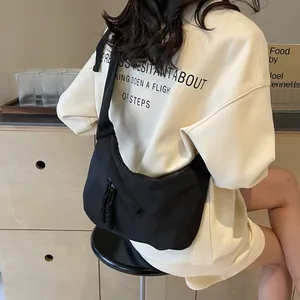 Close-up of black crescent shoulder bag with woven zipper detail worn on beige sweatshirt