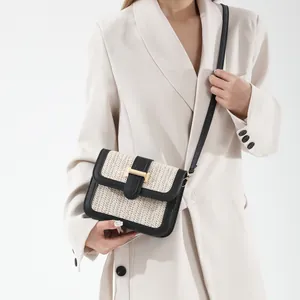 Fashionable woven crossbody bag with black leather trim and gold H buckle on a white suit