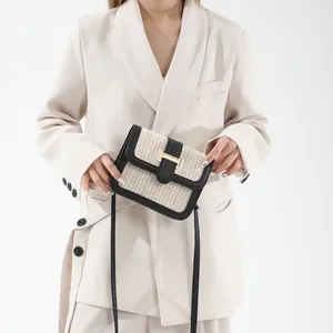 Detail of straw woven crossbody bag with black leather trim and golden metal clasp