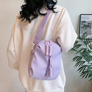 Vista detallada de un bolso bandolera de nailon lavanda llevado por una modelo en casa
