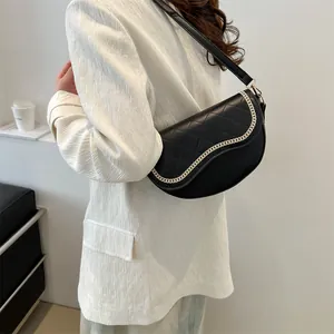 Détail d'un sac selle noir matelassé avec bordure en chaîne dorée et bandoulière en cuir
