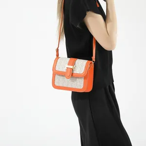 Detail of orange faux leather and woven straw crossbody bag with golden metal bar closure