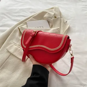 Détail d'un sac selle rouge matelassé avec broderie chaîne dorée et bandoulière