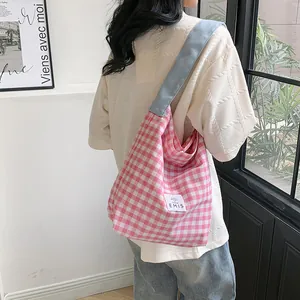 Detail of a pink checkered canvas tote bag with a light blue strap worn by a female model