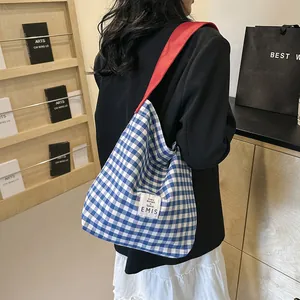 Detail of blue plaid canvas tote with red straps and EMIS label on the side