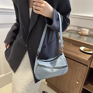 Detail of light blue denim baguette bag featuring double front zippers and shoulder strap