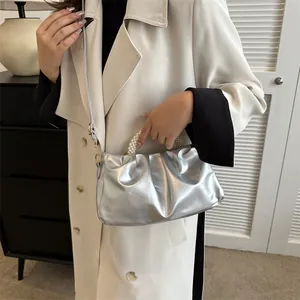 Vue détaillée du sac nuage argenté plissé avec poignée en perles porté avec un trench beige