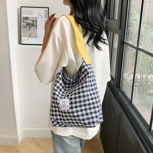 Contrast checkered canvas tote bag with yellow straps shown on a model in a minimalist room