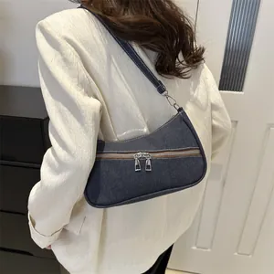 Side view of dark blue denim underarm bag with decorative zippers on a model