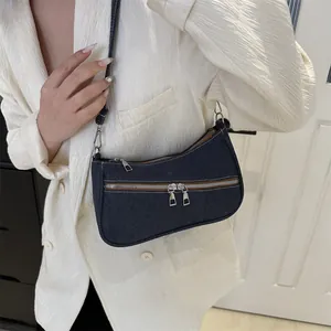 Detail of dark blue denim underarm bag with double zippers and silver metal hardware