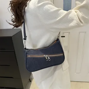 Detailed close-up of dark blue denim shoulder bag with metal double zippers and strap