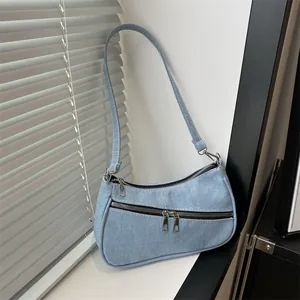 Detail of light blue denim fabric texture and metallic zippers on the underarm bag
