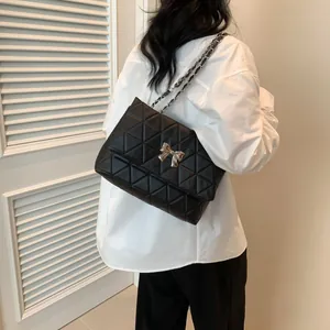 Close-up of black quilted crossbody bag with gold bow clasp and chain strap on a model