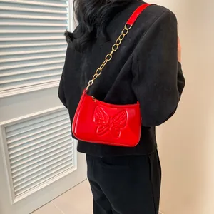 Detail of red patent leather shoulder bag with butterfly embossing and gold chain strap