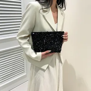 Close-up of elegant black sequined clutch bag held against a white suit for a party look