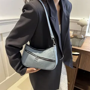 Denim underarm bag in light blue denim, worn with a blazer for a modern urban look