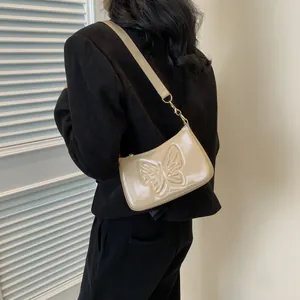 Detail of beige patent leather shoulder bag featuring 3D butterfly embossing and gold hooks