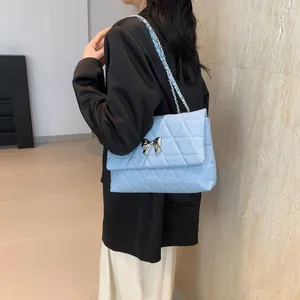 Detail of light blue quilted crossbody bag with silver metal bow and leather chain strap