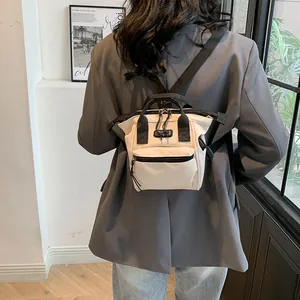 Detail view of a mini canvas backpack with cream body and black straps worn by a model