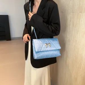 Detail of light blue quilted crossbody bag with metal bow and chain strap