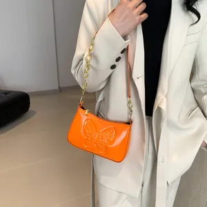 Close-up of bright orange patent leather bag featuring 3D butterfly relief and gold chain