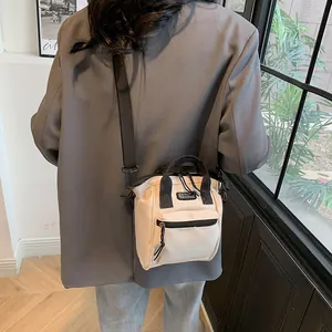 Detail of minimalist cream canvas crossbody bag shown on model in a modern indoor setting