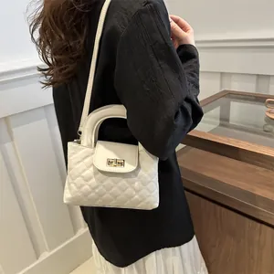 Detail view of a white quilted crossbody bag with golden clasp and leather top handle