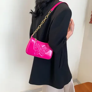 Close-up of fuchsia patent leather handbag featuring butterfly relief and golden chain strap
