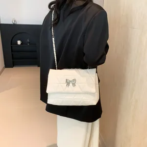 Detail of a quilted cream shoulder bag featuring a silver bow buckle and chain strap