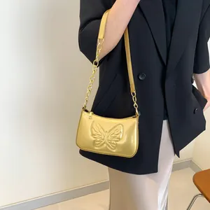 Golden butterfly embossed shoulder bag with metallic chain strap worn by a model