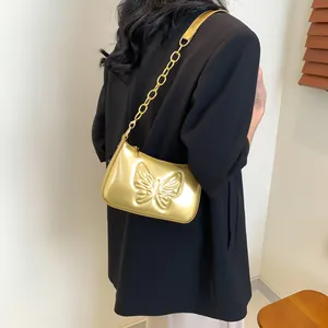 Detail view of a gold metallic butterfly embossed underarm bag on a model shoulder
