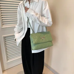 Quilted light green crossbody bag with silver bow and leather chain strap in indoor view